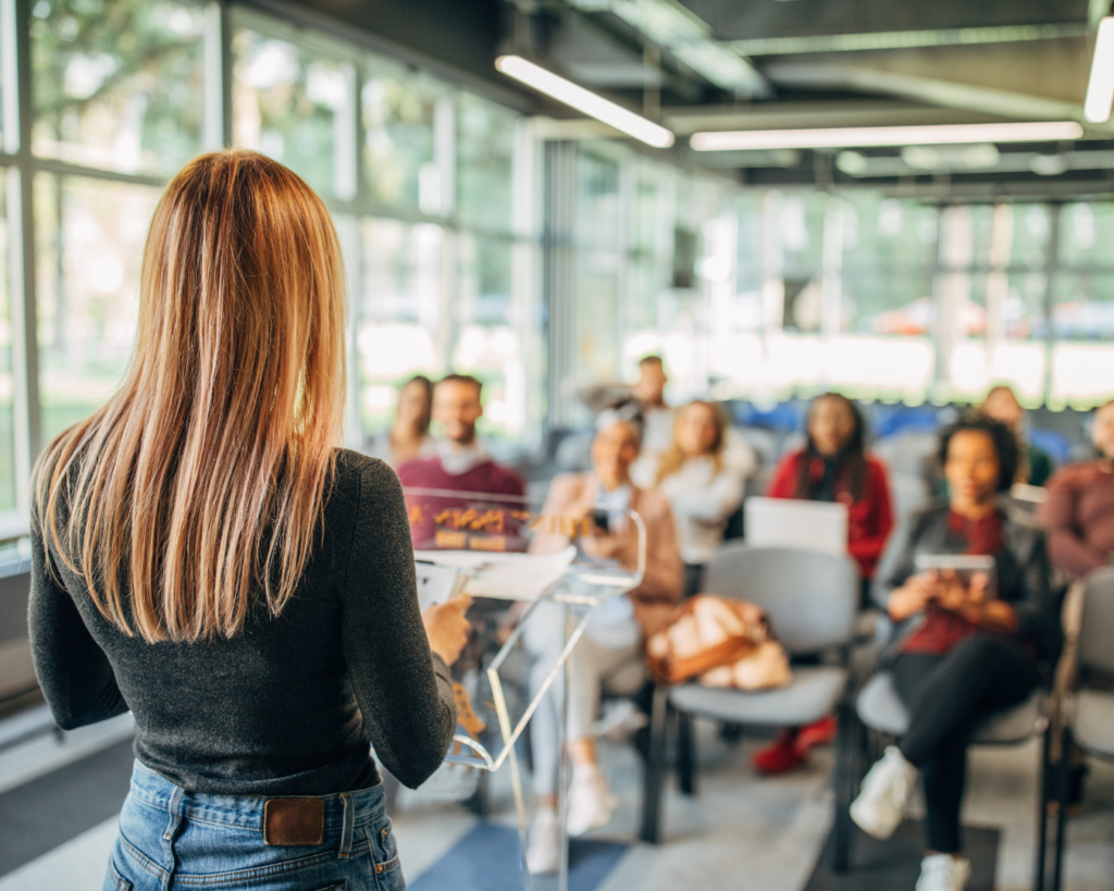 A photo of the back of a woman giving a presentation to a small group of diverse people.
